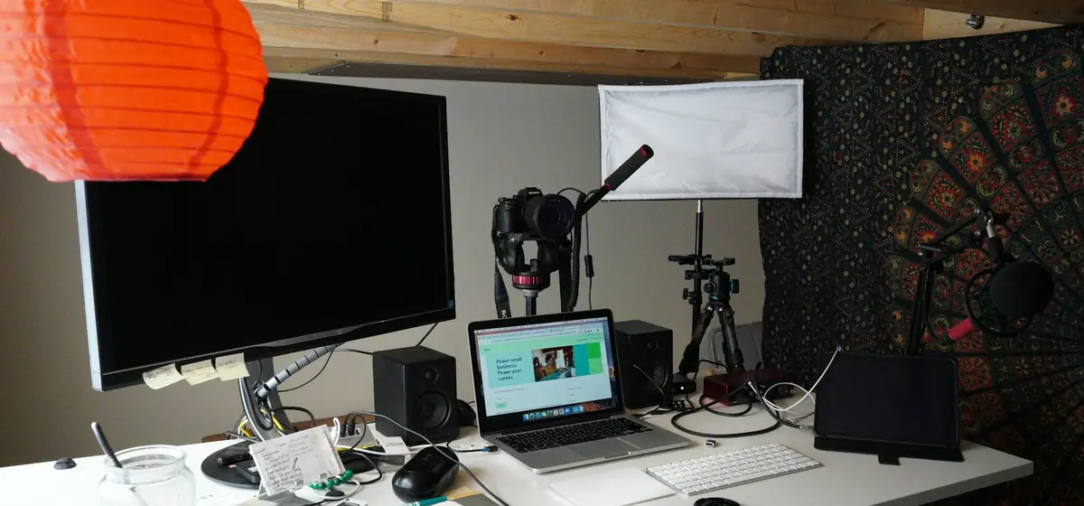 Mesa de trabalho de um criador de conteúdo, com monitor, notebook, câmera e iluminação